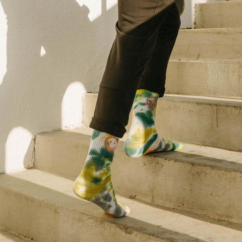 Person wearing Trek Light Happiest Camper Tie Dye socks walking up stairs in sunlight, showcasing comfy and colorful sock design.