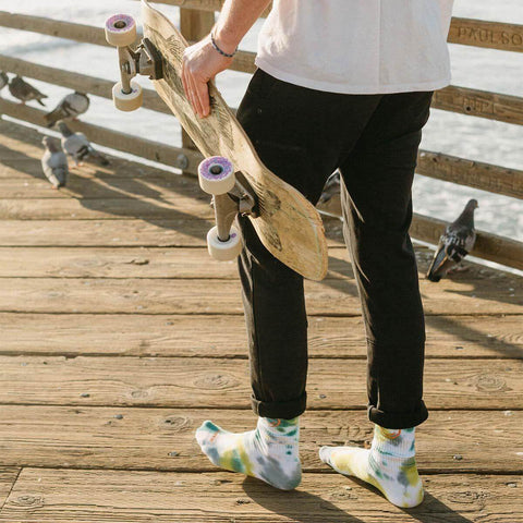 Skateboarder wearing Happiest Camper Tie Dye Socks by Trek Light, standing on a wooden pier by the sea.