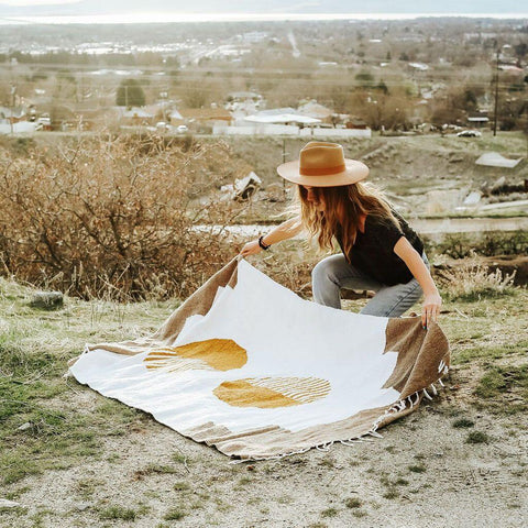 Person spreading Horizon Blanket by Trek Light, handwoven from recycled materials, showcasing sustainable and unique design outdoors.