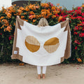 Person holding Horizon Blanket by Trek Light, handwoven from recycled materials, showcasing unique pattern against vibrant floral backdrop.