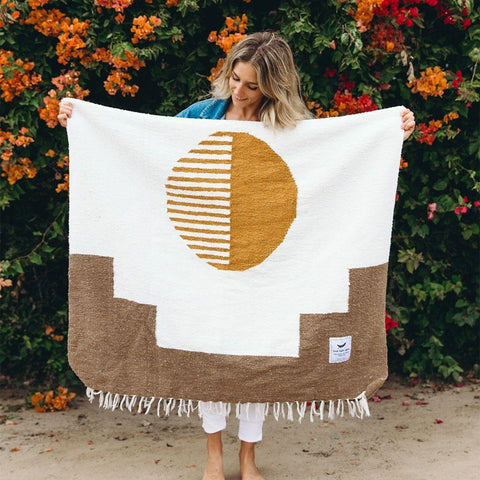 Woman holding the Horizon Blanket by Trek Light, handwoven with recycled materials, showcasing a unique sunburst design.