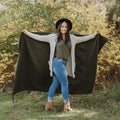 Woman holding Humboldt Blanket, handwoven from recycled materials, standing outdoors with lush greenery. One tree planted per purchase. Trek Light.