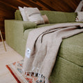 Trek Light Huntington Blanket draped over a cozy green couch, embodying beach vibes and comfort at home.