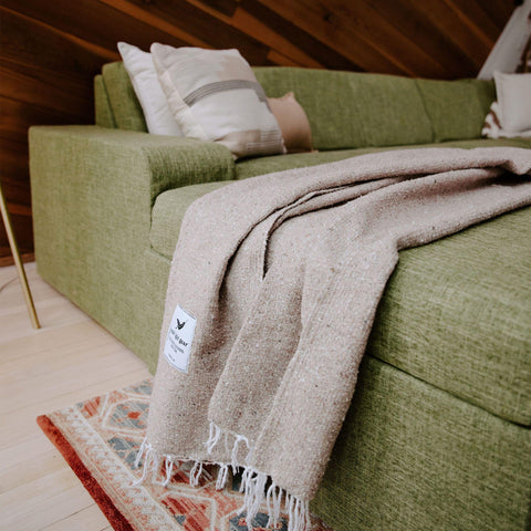 Trek Light Huntington Blanket draped over a cozy green couch, embodying beach vibes and comfort at home.