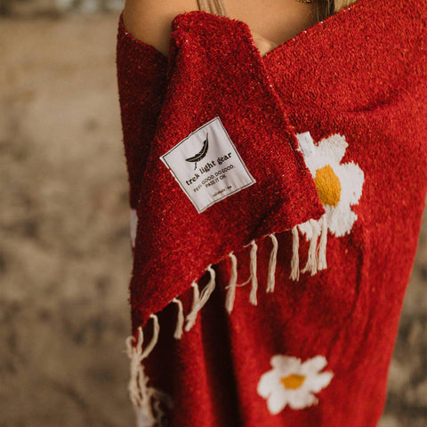 Cozy Lazy Daisy Blanket by Trek Light, wrapped for comfort and relaxation, featuring charming daisy patterns on lush red fabric.