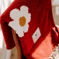 Cozy red blanket with a white daisy design draped over a chair, embodying Trek Light's Lazy Daisy vibe.