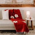 Cozy red Lazy Daisy Blanket draped over a sofa, featuring daisy patterns, perfect for slowing down and relaxing. Trek Light product.