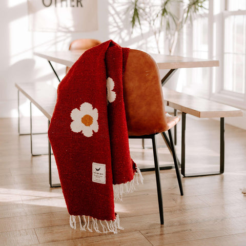 Cozy red Lazy Daisy Blanket on a chair, featuring a charming daisy print. Perfect for slowing down and savoring life's lazy moments. Trek Light.