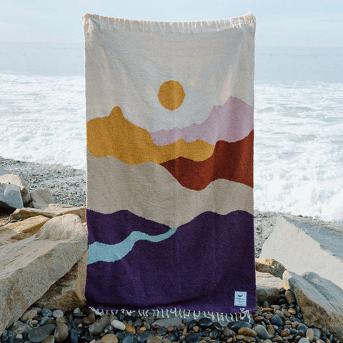 Cozy handwoven Mountain Sunrise blanket made from recycled clothing materials, showcasing beautiful and versatile design by the sea. By Trek Light.