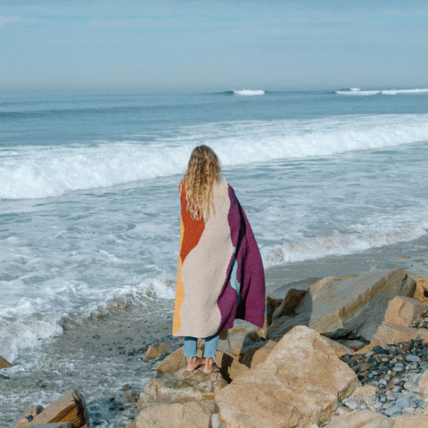 Cozy handwoven Mountain Sunrise Blanket made from recycled materials, perfect for versatility and warmth, by the ocean. By Trek Light.