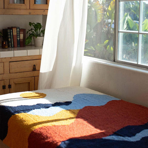 Vibrant handwoven Mountain blanket by Trek Light, capturing sunlight by a window, inviting warmth and artistic flair into your space.