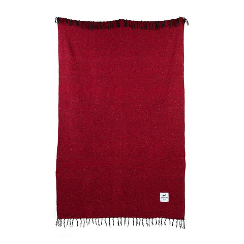 Red handwoven blanket from Trek Light, made with 100% post-consumer recycled materials, featuring a tag and fringe details.