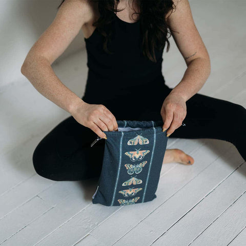 Person sitting on the floor opening a stylish Trek Light pouch with moth design, showcasing a trendy and practical accessory.