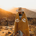 Person wearing handwoven Peace Blanket from Trek Light in a scenic desert sunset, made from recycled clothing, cozy and beautiful.