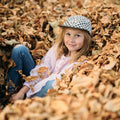 Child wearing a Peace Checkered Kids Hat by Trek Light, smiling and sitting in autumn leaves. Perfect accessory for cool kids.