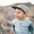 Smiling child wearing a Trek Light Peace Checkered Kids Hat outdoors, showcasing fun style for cool kids.