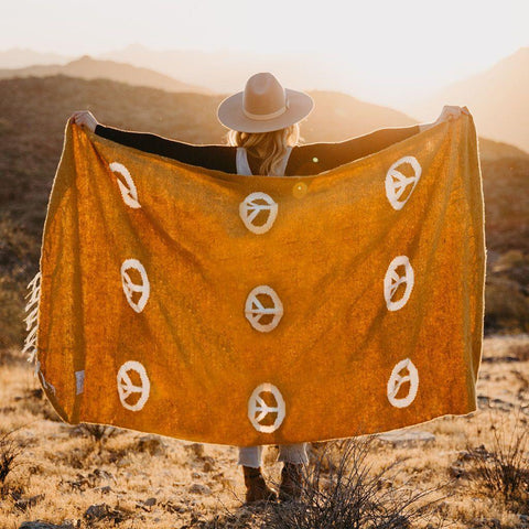 Person holding a handwoven, beautiful Peace Blanket made from recycled clothing materials by Trek Light in a scenic outdoor setting.