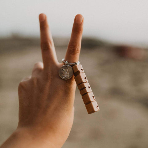 Hand holding Trek Light PEACE wood keychain with nickel hardware, perfect gift idea. Engraved letters spelling PEACE. Boho style accessory.
