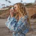 Person in a cozy Sky Dye Robe enjoying photography by the beach. Embrace comfort with Trek Light's unisex fit and sustainable design.