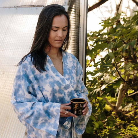 Woman in Sky Dye Robe enjoying morning coffee outdoors with Trek Light ethos, embracing sustainable and comfortable unisex style.