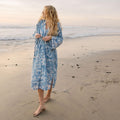 Woman in a blue robe walking on the beach at sunset, embodying the Trek Light lifestyle.