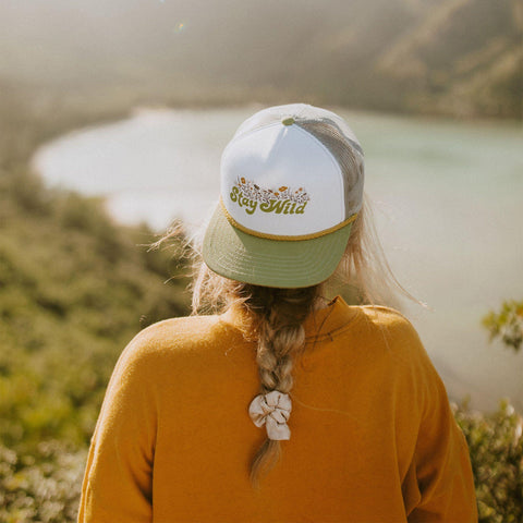 Back view of person wearing a Stay Wild foam trucker hat facing a scenic landscape by Trek Light.