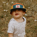 Toddler wearing colorful Stay Wild Trek Light kids hat, perfect for outdoor adventures. 5-panel camper style. Youth sizes available.