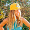 Woman wearing yellow "Take It Easy" snapback hat by Trek Light in nature, flat brim, unisex style, supports tree planting initiative.