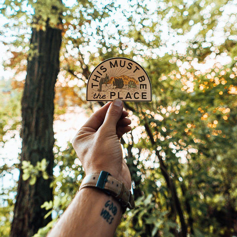 Trek Light This Must Be The Place mountain sticker held in the forest, capturing the essence of adventure and nature.