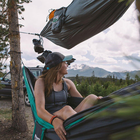 Woman relaxing in Trek Light VersaTrek hammock with mountain views, showcasing its versatility as a swing and gear loft.