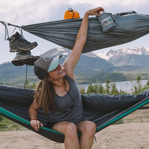 Person relaxing in a Trek Light VersaTrek hammock with shoes and gear, enjoying the outdoor mountain view. Versatile mini hammock.