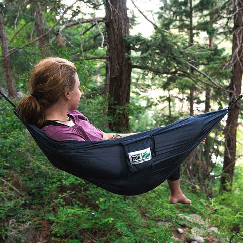 Person relaxing in a Trek Light mini hammock amidst lush green forest, showcasing the versatility of the 8oz VersaTrek gear.