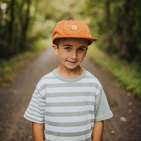 Child wearing "You Are My Sunshine" orange kids hat, standing on a forest path. Trek Light kids snapback for outdoor adventures.